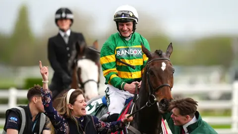 PA Media I am Maximus after his 2024 Grand National win, with jockey Paul Townend in green and gold on the horse and and three others around it on the ground