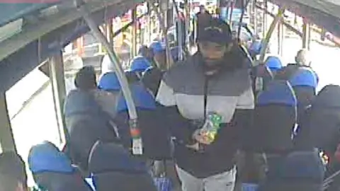 West Yorkshire Police Man wearing a striped puffa-style jacket and a baseball cap walks down the aisle of a bus
