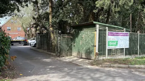 Martin Heath/BBC Exterior of the entrance to a nursing home, with the two-storey brick-built home at the end of a drive. Cars are visible in front of the home. There are trees to the right of the entrance alongside a small green outbuilding. A notice that the home has received a Good CQC rating is attached to a fence to the right.