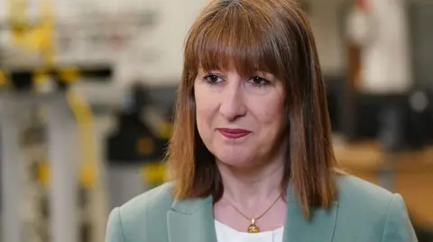 Getty Images Chancellor Rachel Reeves wearing a light green jacket and white top standing in front of a blurred background