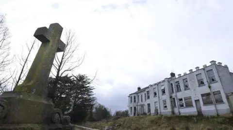 Getty Images The former Marianvale Mother and Baby home in Newry. A dilapidated two-storey building surrounded by overgrown grounds and a holy cross plinth.