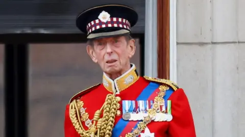 The Duke of Kent in a regal red royal uniform.