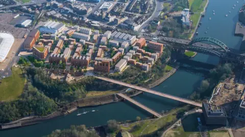 A CGI image shows what the residential community could look like. Blocks of flats overlooking the River Wear are interjected with green spaces. A footbridge connects the homes to the other side of the river. The homes are situated between the Stadium of Light and the Wearmouth bridge. 