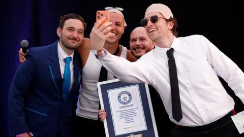 PA Media Guinness World Record ajudicator Will, content creator Jack Remmington, Pitbull and BBC Radio 1 Breakfast presenter Greg James pose for a selfie photo.