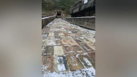 Danijel Borna Fiket A long path of brick in beige, brown and red colours. It is surrounded by a short wooden fence. Parts of the bricks are covered in snow. 