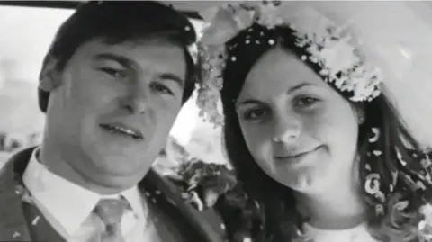 Sandra Francis Black and white wedding photo of a man in a white collar suit and a woman wearing a flower veil. Both have confetti in their hair and on their shoulders 