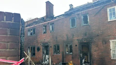a close up of homes burned in a fire - windows and doors are smashed with black soot all over the buildings 
