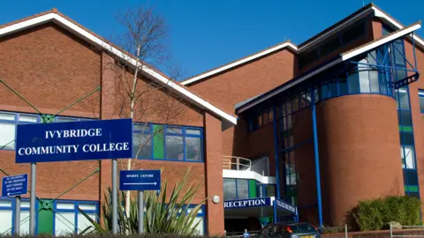 Alamy Ivybridge Community College, a red-brick post-modern building which appears to date from the 1980s or 1990s, with angular pitched roofs, curved brickwalls, blue window frames and green accents.