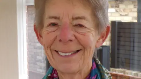 A smiling Judith Boichot. She has grey hair and is wearing a multicoloured scarf.