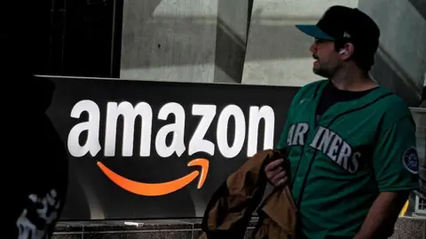 Getty Images A man wearing a green top walks past an Amazon sign on a street