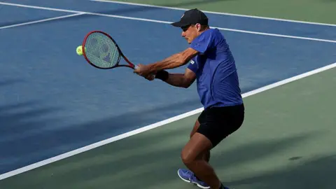 Getty Images Kamil Majchrzak pictured wearing a blue t-shirt, black shorts and a black cap. He holds a tennis racket in his hand.