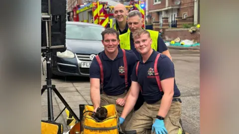 The rescued cat alongside firefighters in front of a fire engine