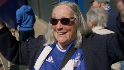 Woman in shades and Ipswich Town kit smiles. 