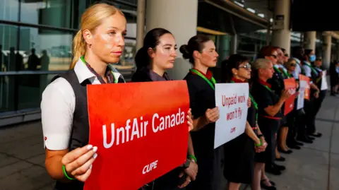 Carlos Osorio / Reuters Air Canada Air Canada Asperts sign at Toronto Pearson Airport "Canada is unfair" and "Unpaid jobs won't fly". They stood in a line, wearing uniforms.