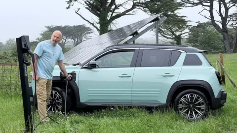 A man charging a car with an electric vehicle charger that's connected to a solar panel.