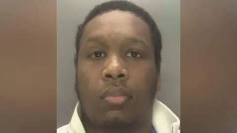 Custody image of Said Daauud a man with short black hair and a goatee. He is wearing a white shirt and looking at the camera.