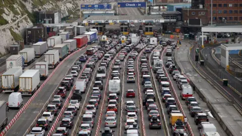 Getty Images Cars queue at the border while waiting to board ferries at the Port of Dover in 2023. There are eight lanes of traffic leading up to the port and on the left hand side there are two lanes of lorries queuing. A road sign with the words