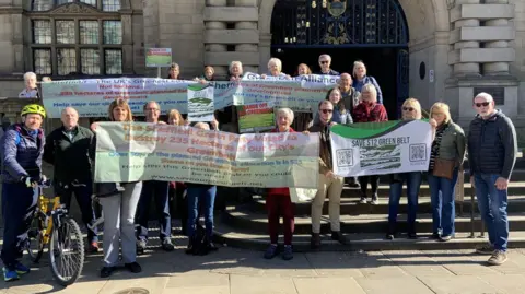 A group of people are gathered with banners and placards outside Sheffield town hall