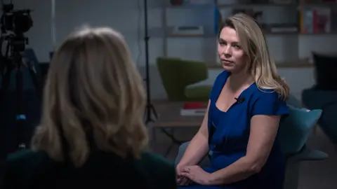 Emma Lynch / BBC Sara Veen -Win -Villiams - a woman with long blonde, wearing a blue dress - sits on a chair in front of BBC's Katie Razal, which is back into the camera.