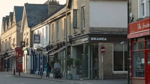 A view of Jericho's Walton Street businesses such as The Jericho Cafe and Branca restaurant. People can be seen walking in front, one man is pushing a pram.