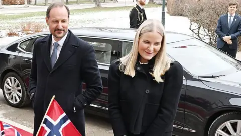 Corbis via Getty Images A couple in black coats stand in front of a car with a Norwegian flag waving in the foreground