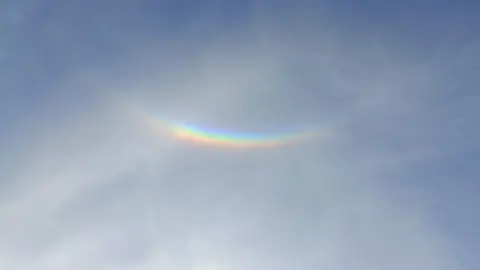 Rachel Sanders An upside down rainbow which is an optical illusion, seen against a blue sky with wisps of white clouds. 