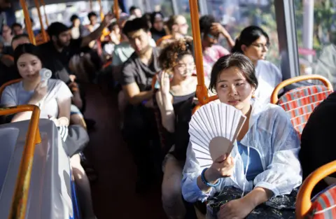 EPA A person uses a fan to cool down on a TfL bus which is busy with other passangers