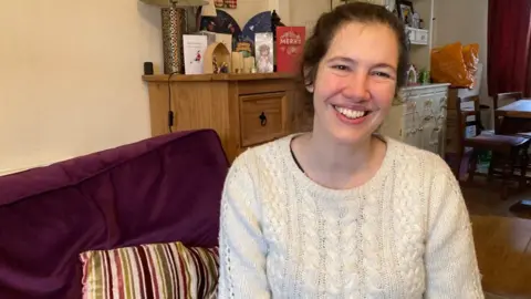 A woman is sitting on a purple sofa, smiling at the camera
