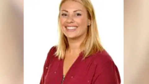 BBC Posed headshot image of vicki williams wearing red blouse and smiling. She has long blonde hair