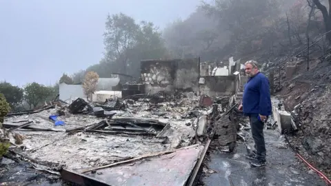 Matthew Ferraro berdiri di sebelah rumahnya, yang telah dibakar ke tanah, di Topanga Canyon