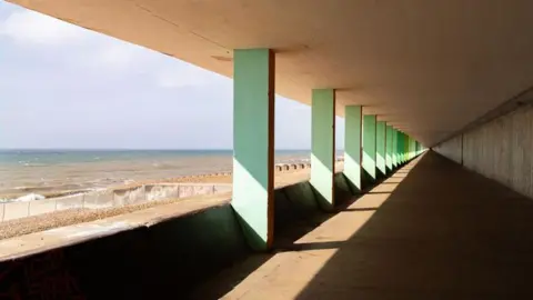 Hastings Bottle Alley runs along the seafront, with a view of the beaches and waves through the columns rectangular columns. The back wall has pieces of bottles embedded into it. 