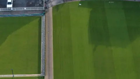 An aerial view of a tennis court. There are deep lines running across the lawn.