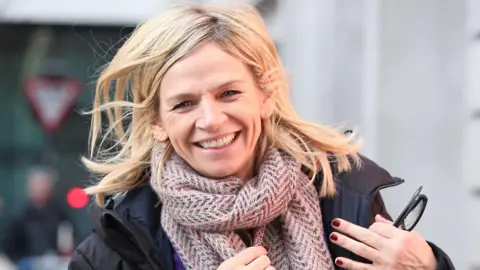 Getty Images Zoe Ball smiling in a black jacket and brown scarf.