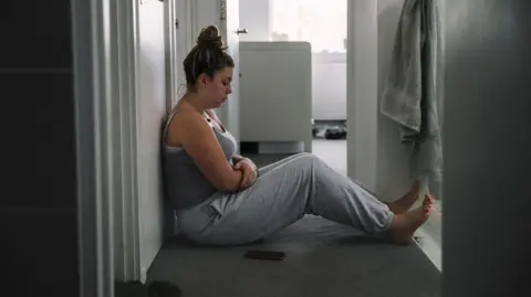 A young woman sits in the hallway of her home looking sad and lonely