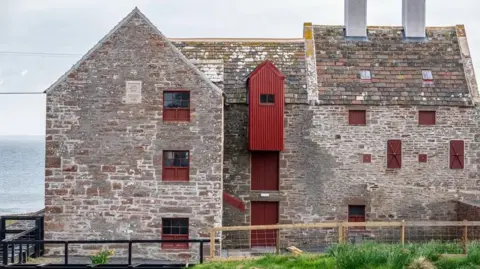 A large stone three storey building with window shutters painted a rusty red colour