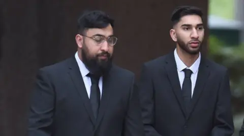 PA The two men wear black suits with white shirts and black ties.