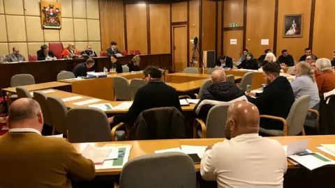 A back view of councillors and officials at a Pendle Council meeting with the mayor and four other people facing them from a raised stage.