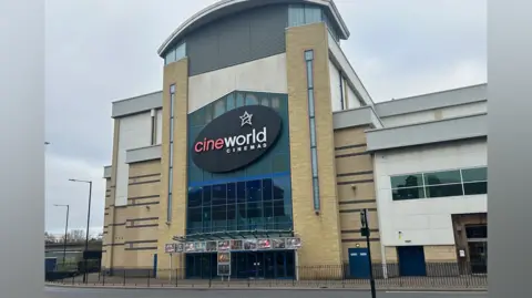 BBC The Cineworld in Middlesbrough is a four-storey light brown brick building. The black sign at the front reads: "Cineworld Cinemas". Underneath are posters with various movies advertised.