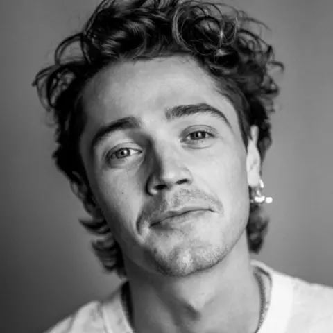 Henry Rowley Black and white picture of a young man with curly hair and stubble