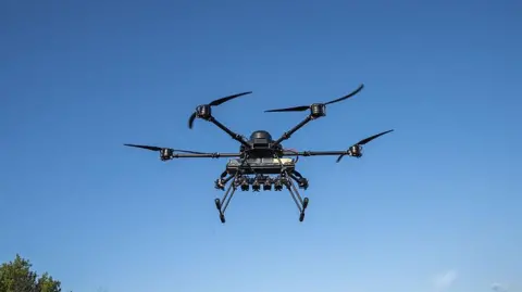 Getty Images A view of a Vampire and Kamikaze BC drone used by the 59th Brigade during tests before deployment to the frontline in Dnipro, Ukraine on May 21, 2025. The drone has four prongs and is flying in a blue sky.