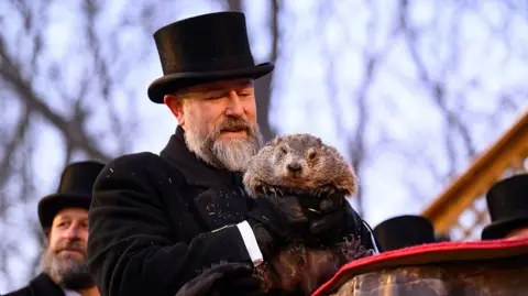 Groundhog handler AJ Dereume, wearing a black top hat and black coat, holds Punxsutawney Phil