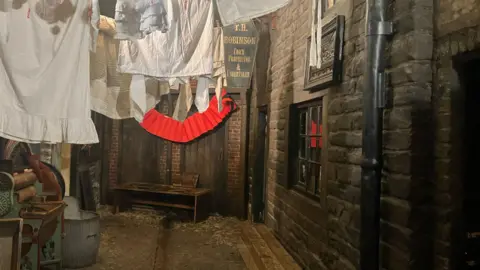 BBC / Elizabeth Baines Cobbled streets are lined by a York stone terraced row. Laundry loads are strung up above the streets.