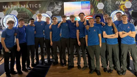 Elliot Deady A group photo of 15 boys, all in blue school-branded T shirts with their arms around each other
