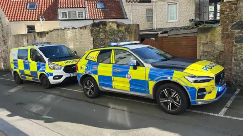 Two police cars, parked outside. They are yellow and blue painted.