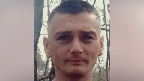 A headshot of a man with short cropped dark hair, looking into the camera