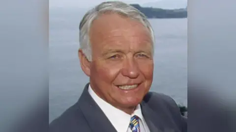 Craig Rich smiling towards the camera with the sea in the background.