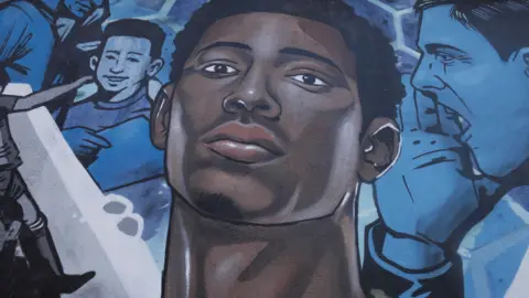 A street art painting of Jude Bellingham, wearing an England shirt, with other footballers painted in blue surrounding him on a Stourbridge wall