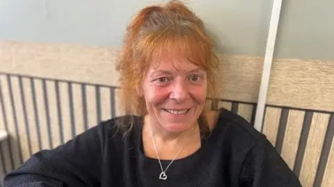 Michelle Cornock is a resident in Immingham. She is smiling into the camera as she talks about local election issues. She has red hair tied up into a pony tail and she's wearing a black jumper with a love-heart necklace. She is sat in a cafe, at a table with her back to the wall.