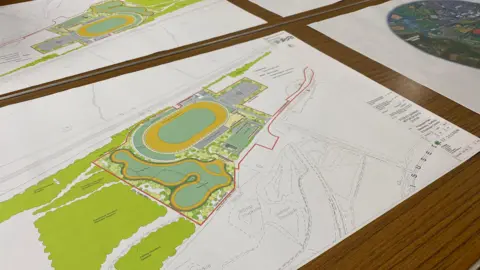 Aerial-view digital plans of the new stadium on a table, showing a track and greenery