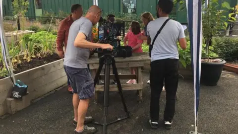 Alfreton Park School The back of a man holding a camera who is filming pupils and presenter Justin Fletcher